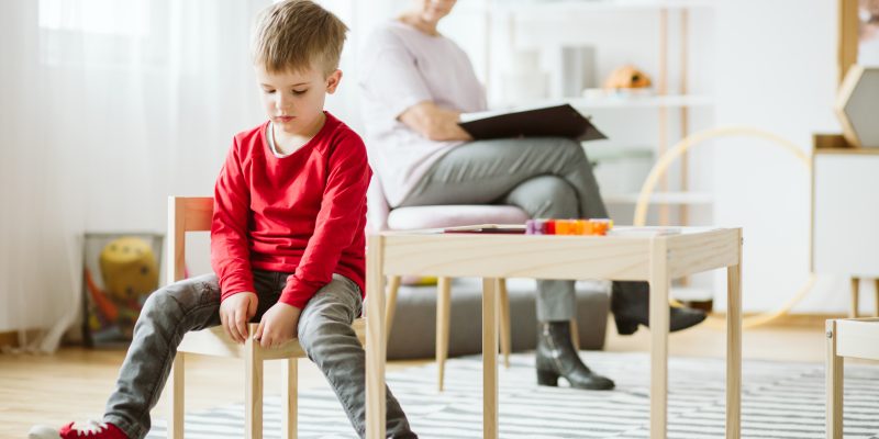 Niño con autismo sentado en una silla en un salón de clases en terapia