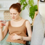 Retrato de mujer joven que sufre de dolor de estómago tomando analgésicos en casa, espacio de copia