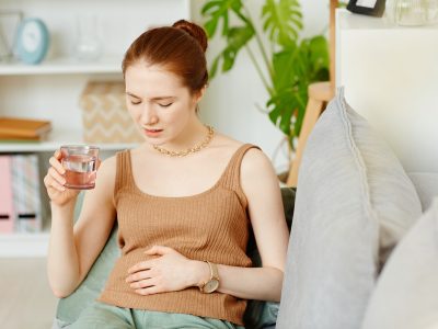 Retrato de mujer joven que sufre de dolor de estómago tomando analgésicos en casa, espacio de copia