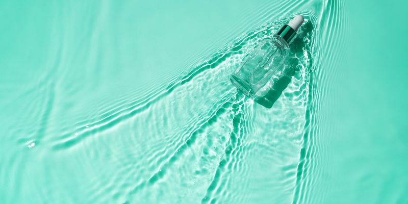 Suero hidratante con ácido hialurónico en una botella transparente con una pipeta sobre fondo azul agua Fondo médico para el cuidado de la piel de belleza. El concepto de hidratación express rápida